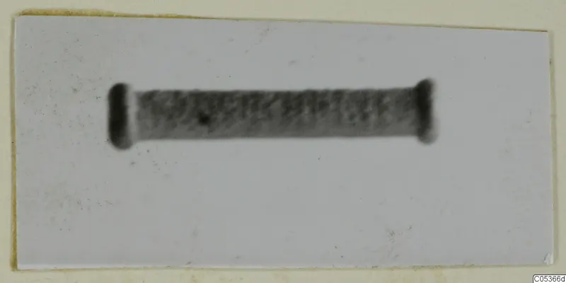 Silver artefact: a blurred dark grey cylinder with rounded ends, shown against a pale plain background