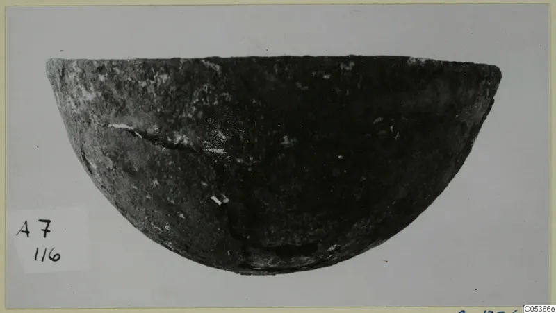 Dark, rounded bowl with a cracked side, photographed against a pale grey background from Amathus tombs 1-9