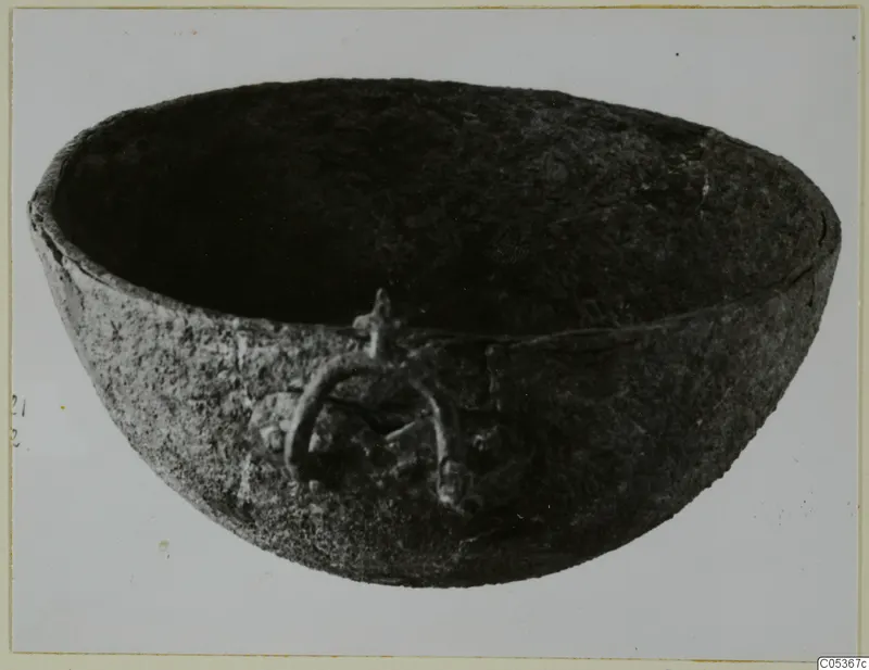 Dark, rounded bowl with a ring handle on its side, photographed on a pale background