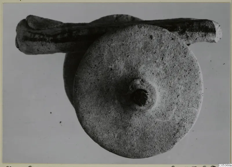 Stone object from Amathus: a round flat disc with a central boss and hole, with an elongated stone piece behind it