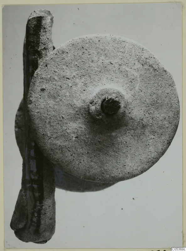 Round grainy disc with a central boss beside a long rod-shaped object, on a pale background