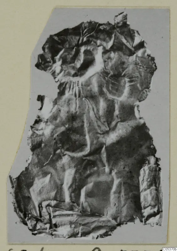 Crumpled fragment of thin embossed metal sheet from Amathus, mounted on grey card.