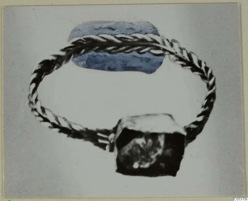 Gold jewellery fragment from Amathus: a twisted-wire loop with a blue oval element and a dark block.
