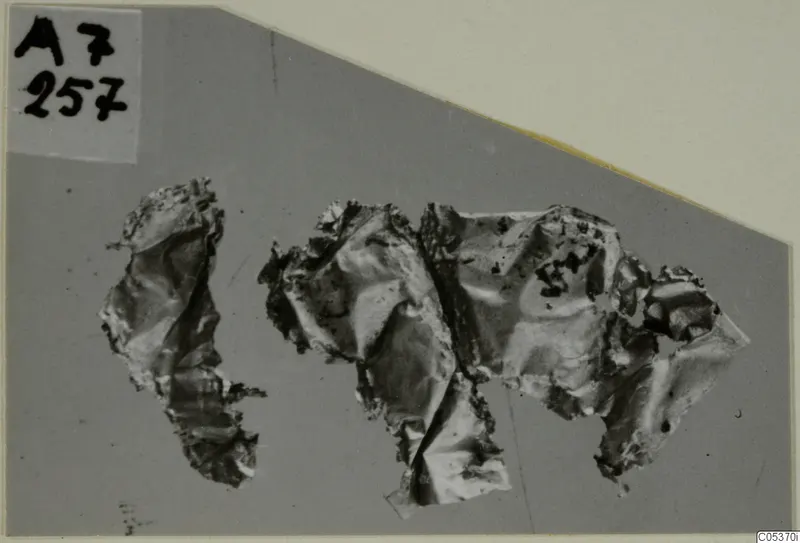Crumpled fragments of thin gold sheet jewellery on a grey backdrop