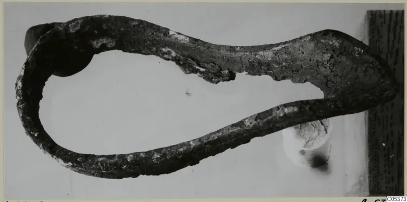 Corroded metal object curved into an open loop with a flattened end, from Amathus, photographed on a plain background.
