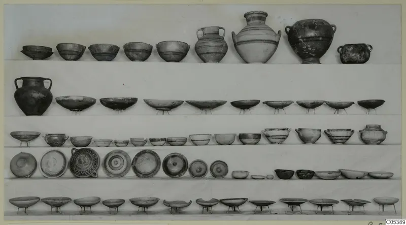Rows of pottery bowls, handled jars and dishes set out on shelves, Amathus Tomb 16.