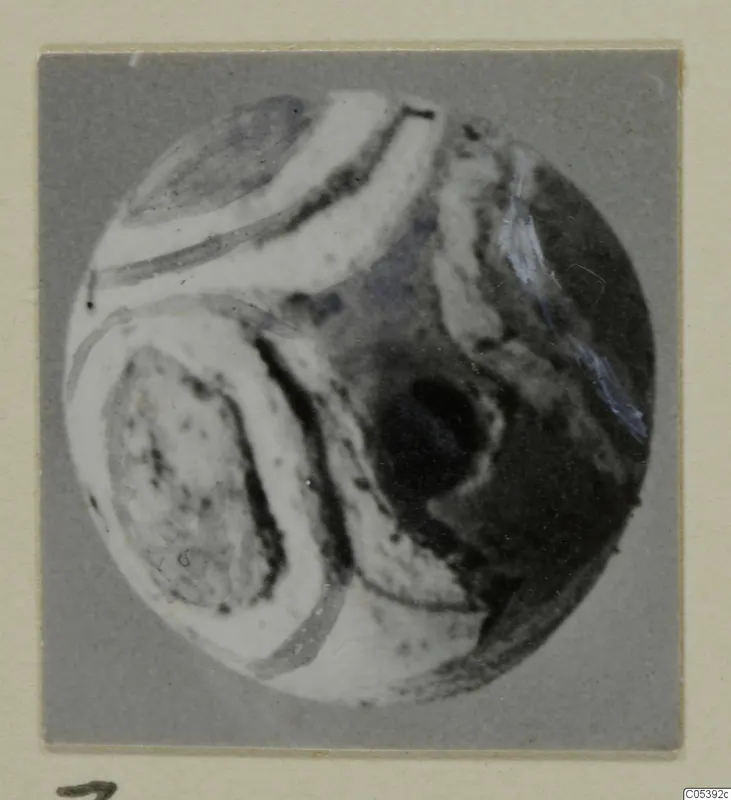 Round object with curving white bands and dark patches, photographed on a grey mount, from Amathus tombs 2-26