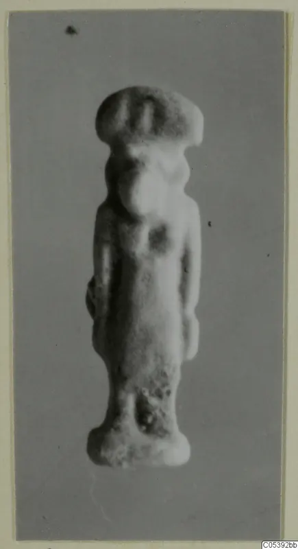 Small standing figurine with a wide flat-topped headdress, photographed against a grey backdrop, from Amathus
