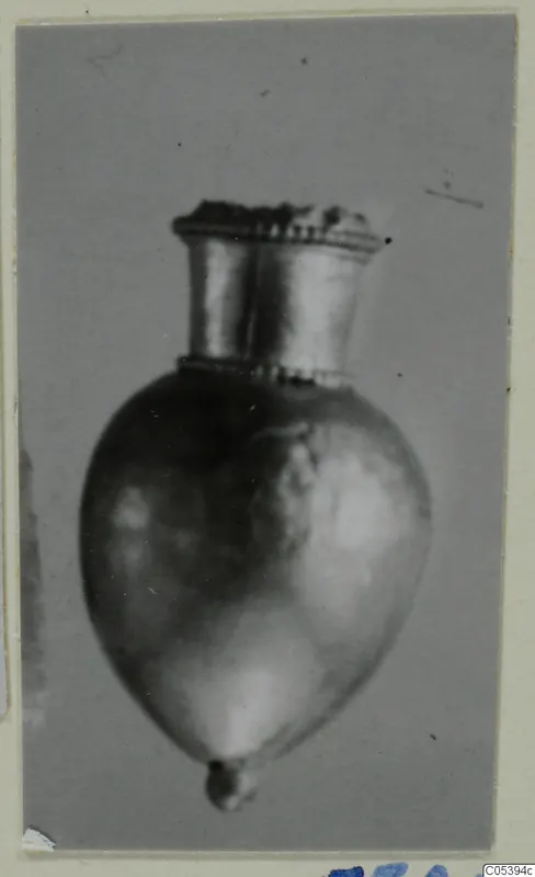 Single small metal object with a flared neck and rounded body, shown against a grey backdrop