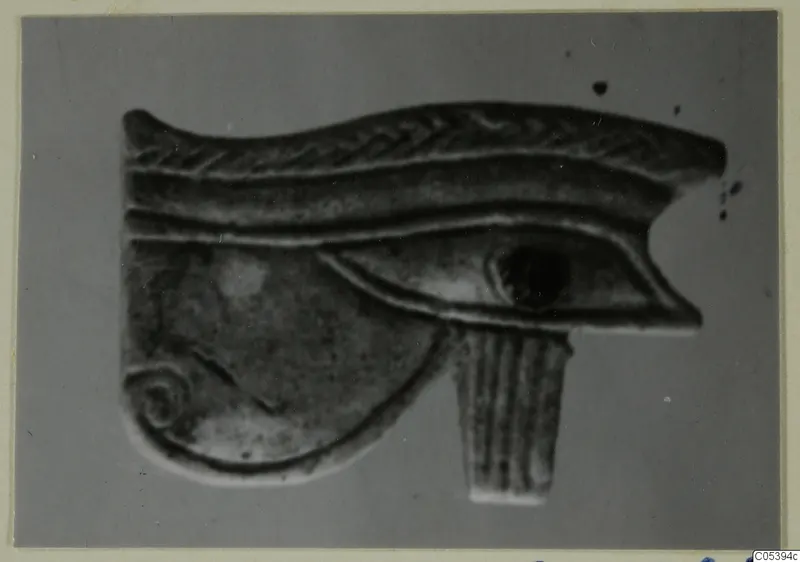 Eye-shaped jewellery piece with a spiral curl and a fluted tab below, photographed against a grey background.