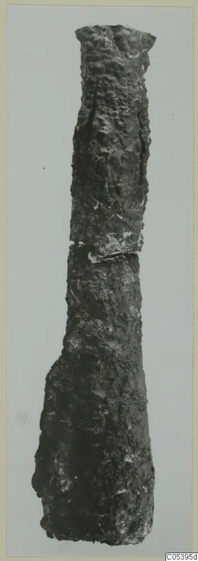 Long, heavily corroded iron weapon fragment from Amathus, standing upright against a pale grey background