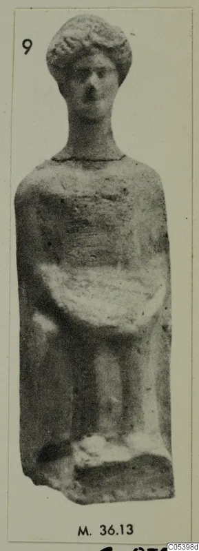 Small terracotta standing figure with curled hair and bent arms, shown on a mounted photograph.