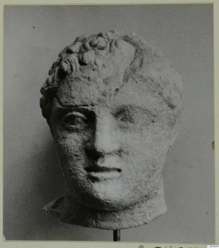 Sculpted head from Mersinaki with short curled hair, pale stone-like surface, mounted on a thin metal stand
