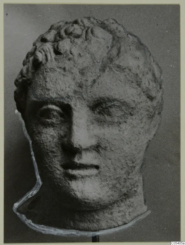Carved stone head with short curly hair, from Mersinaki, shown frontally on a stand