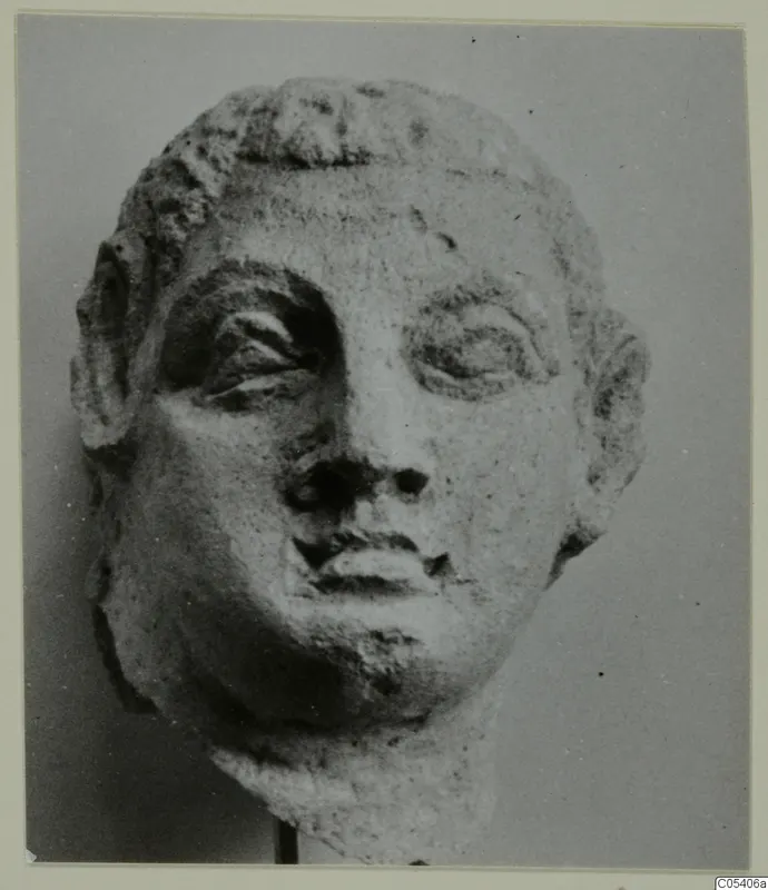 Sculpted head from Mersinaki with curled hair over the forehead, heavy-lidded eyes, prominent ears and a broken neck.