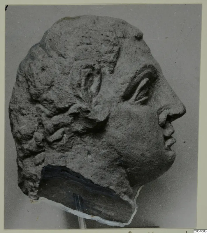 Profile photograph of a carved stone head from Mersinaki, facing right, with wavy hair and a pitted surface.