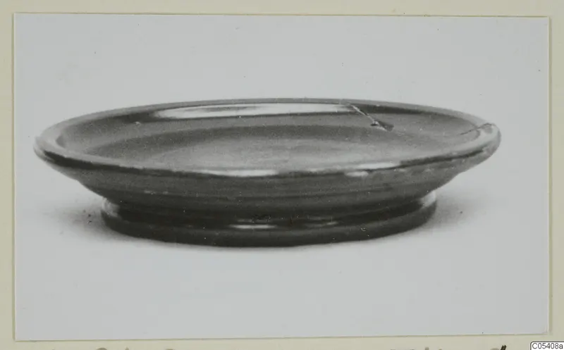 Shallow black-glazed bowl with a flaring rim and a ring foot, photographed from the side.