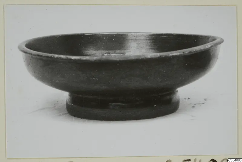 Black glazed bowl with a low ring foot, photographed in side view.