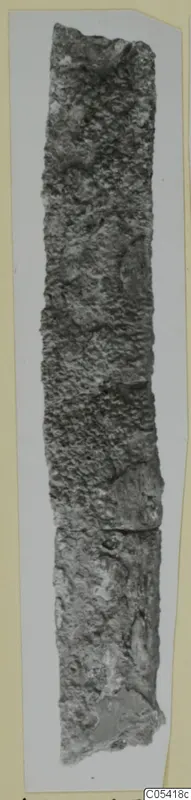 Long, narrow iron tool from Amathus, heavily corroded and encrusted, shown upright on a grey card.