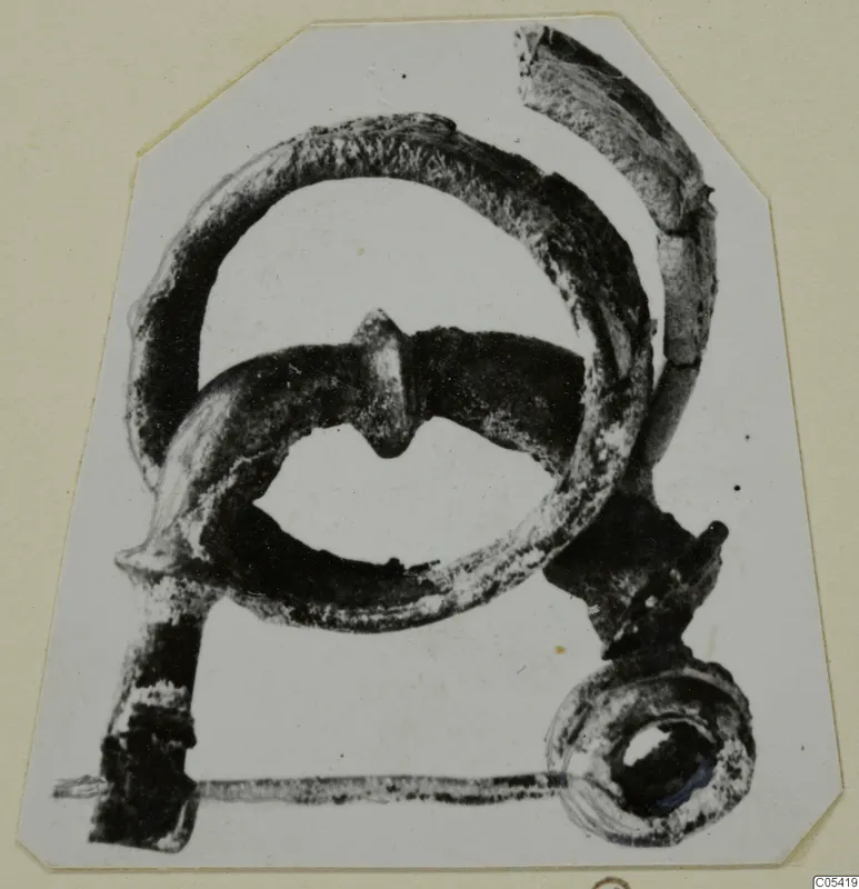 Corroded metal object from Amathus, tomb 2-26, with a large loop and a ring-shaped end, photographed on a card mount