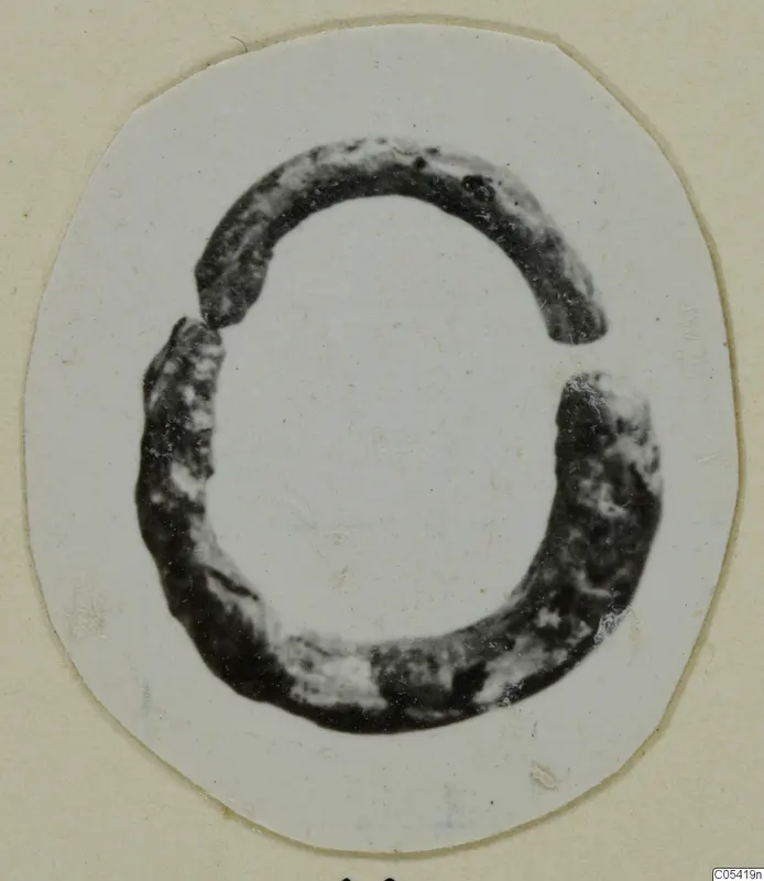 Dark, corroded open ring with a gap at the top, shown as a cut-out photograph on a cream card