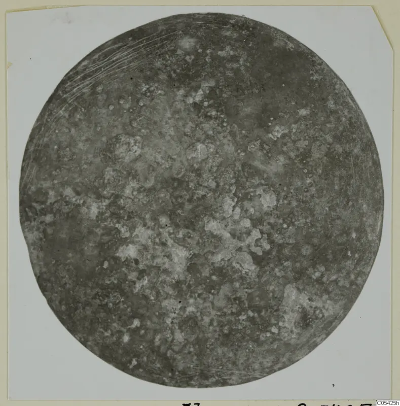 Round, corroded bronze disc from Marion, shown on a white card mount.