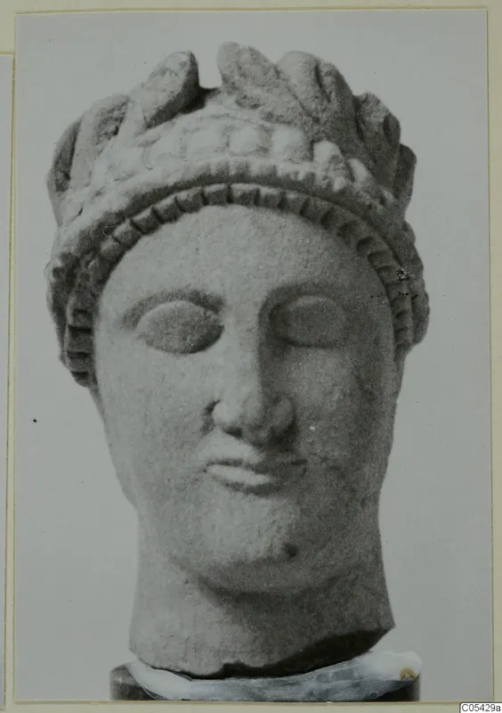 Carved limestone head from Mersinaki, wearing a tall crown of leaf-like forms above a band of dotted ornament.