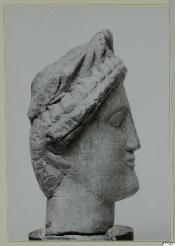 Limestone head from Mersinaki, shown in right profile with a tall layered headdress on a dark base.