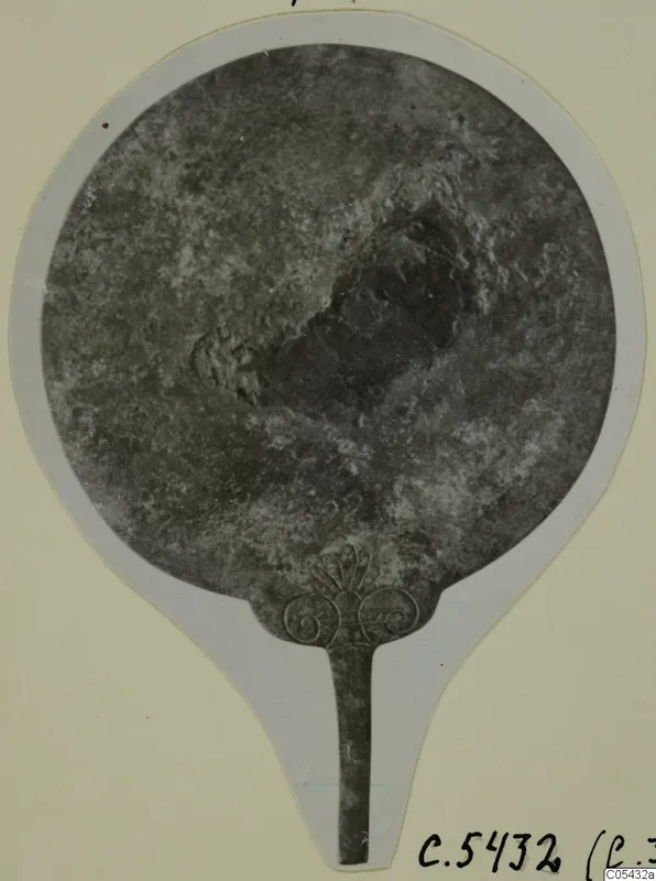 Bronze mirror with a long tang and an openwork palmette-and-scroll finial, from Marion Tomb 57.