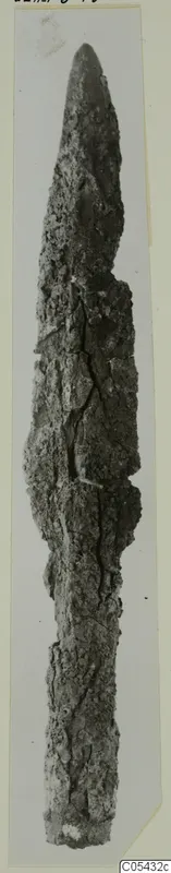 Corroded iron spear-head from Marion, Tomb 68, shown upright against a pale background.