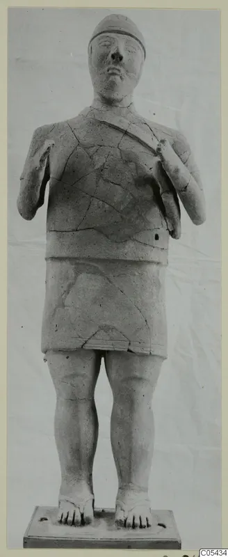 Terracotta Proto-Cypriote I statue of a standing figure with a cap and hands raised to the chest, on a rectangular base.