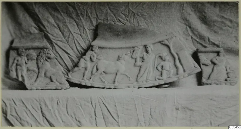Three carved stone relief plaques with figures and animals, including a lion, set on a draped cloth.
