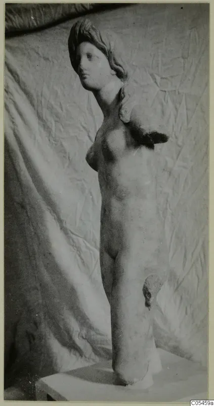 Marble statue of a standing female nude with arms missing, photographed on a plinth against a draped cloth.
