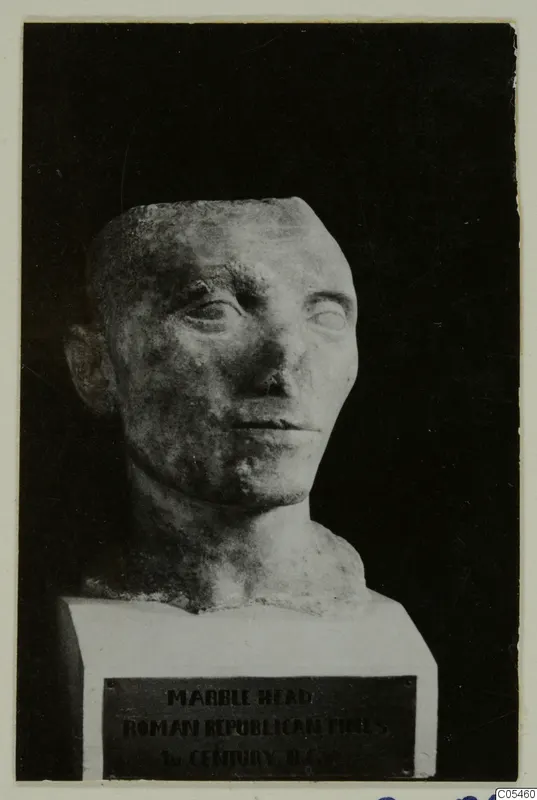 Roman sculpture: marble head with short hair on a white plinth, against a dark background