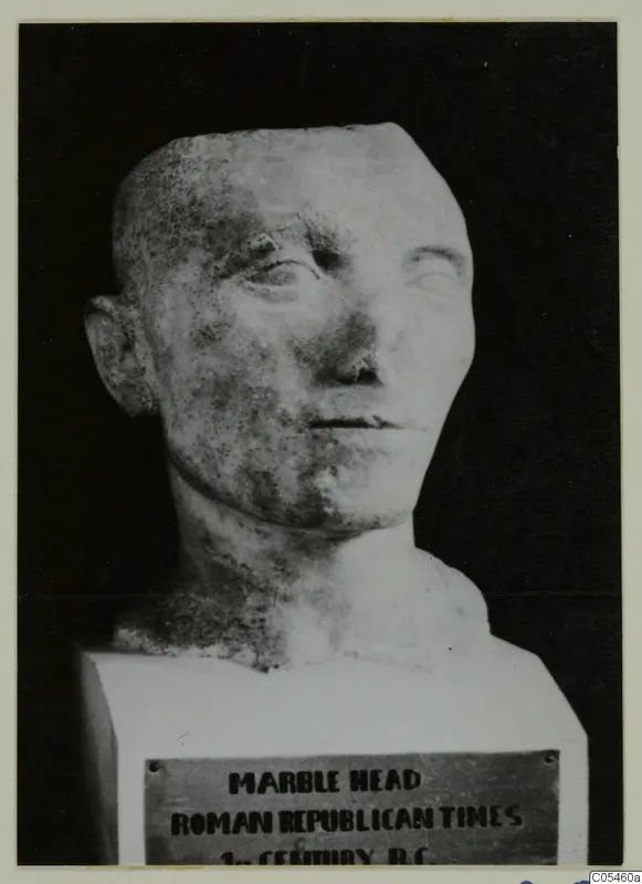 Stone head sculpture on a square block base, with a printed plaque on the front of the base.