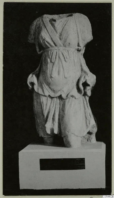 Marble sculpture of a headless standing figure in a belted tunic, shown on a plinth against a black background.