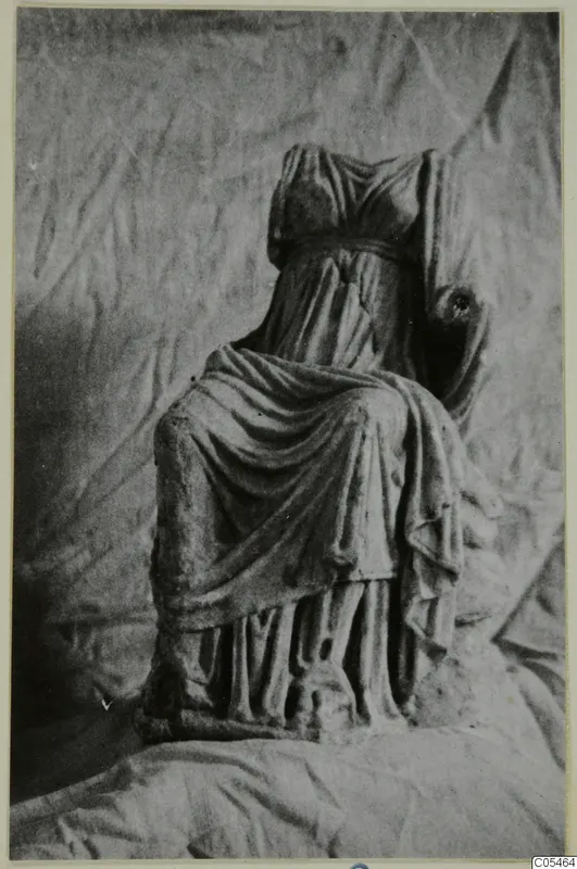 Headless marble sculpture of a seated, draped figure, photographed against a crumpled cloth backdrop