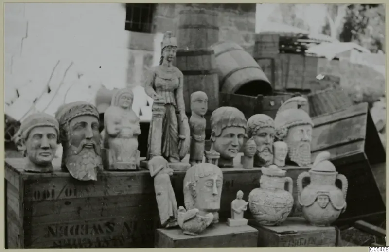Sculpted heads, a standing statue and two lidded two-handled vessels set out on wooden crates outdoors