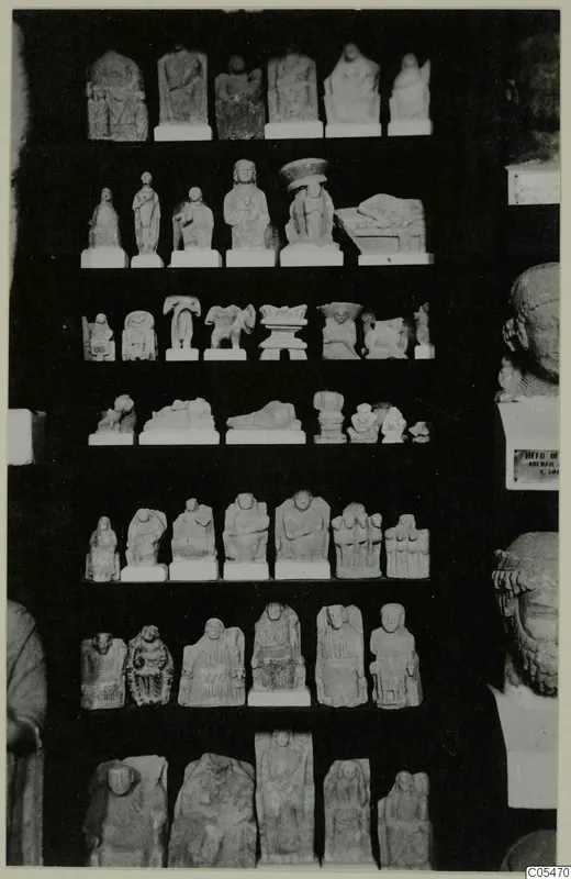Rows of small limestone figurines and reliefs on shelves against a dark background, with large stone heads at the right edge.