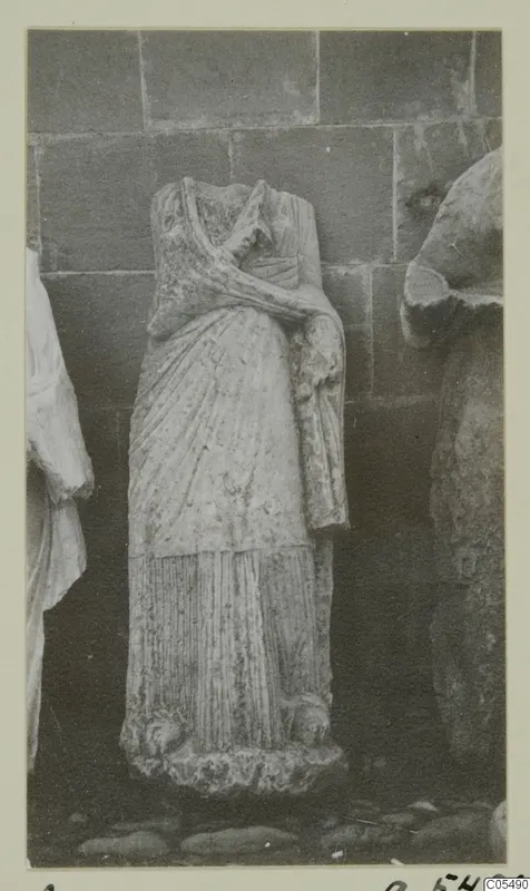 Headless draped stone statue of a standing figure, Arsos, photographed against a block wall