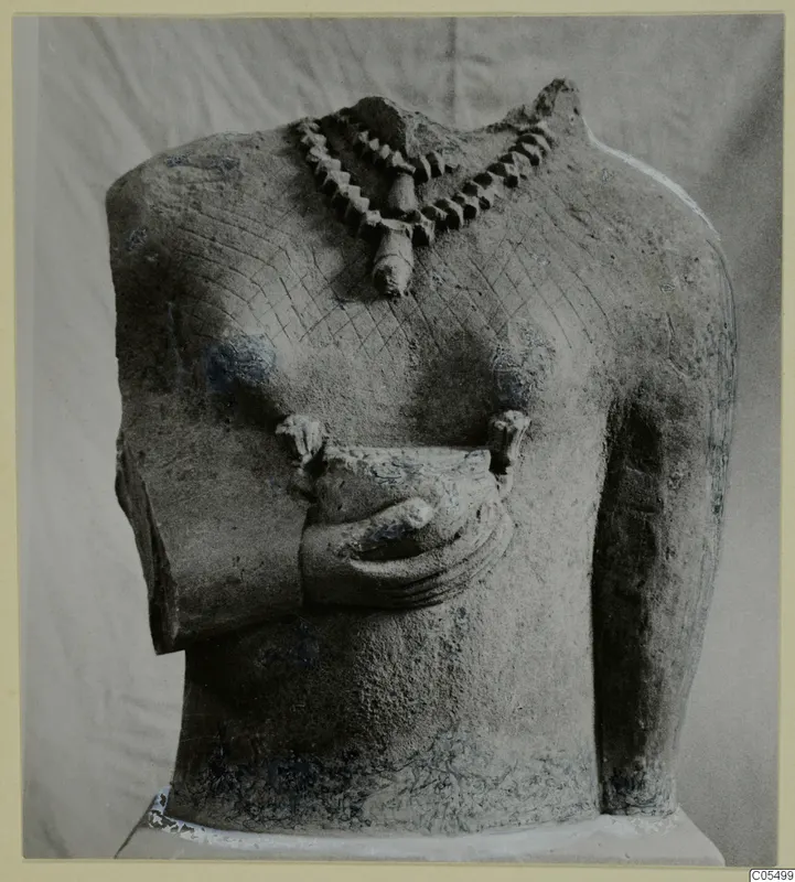 Headless limestone statue torso with a necklace, cross-hatched chest and one hand held at the waist.