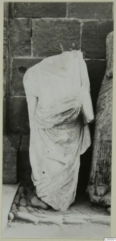 Headless draped marble statue standing against a wall of large stone blocks