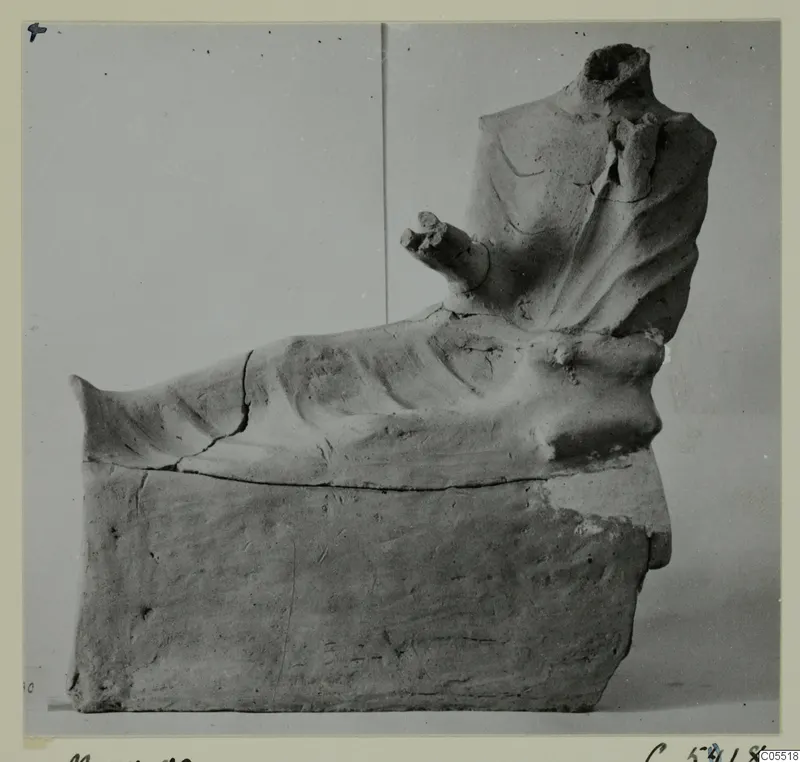 Terracotta figurine of a headless seated figure on a block base, one arm stretched forward