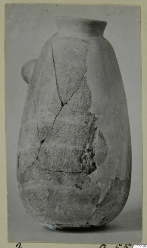 Pottery vessel from Amathus, tall with a flared rim and a small side handle, cracked and partly broken.