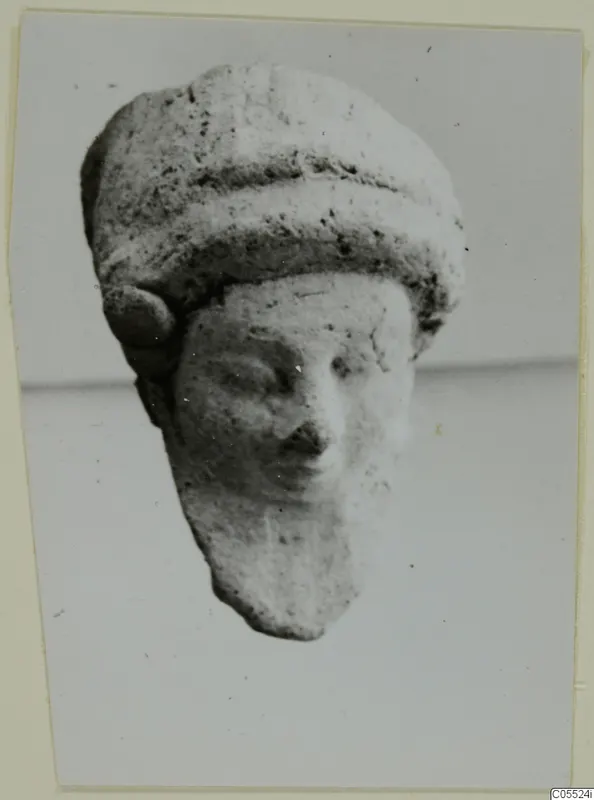 Terracotta figurine head with a tall banded headdress and a worn face, from Mersinaki
