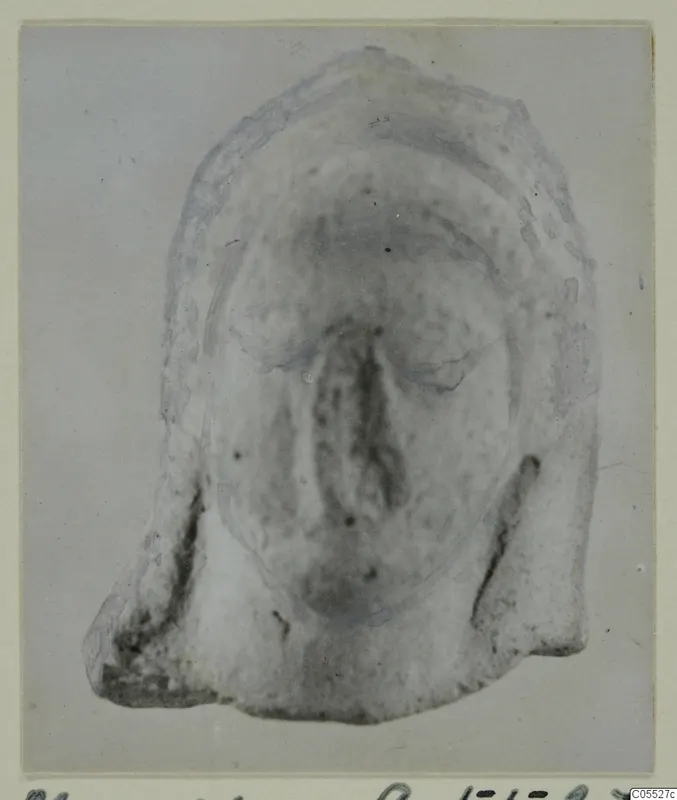 Front view of a fragmentary terracotta figurine face, the broken lower edge visible