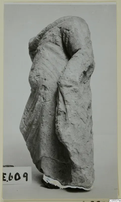 Headless draped stone figure from Mersinaki, photographed against a plain grey backdrop.