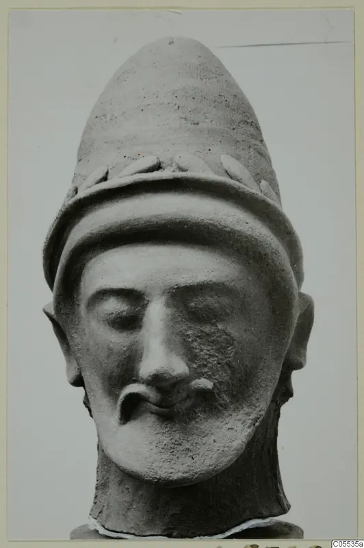 Terracotta head of a bearded man wearing a tall conical cap with leaf-like ornament, from Mersinaki