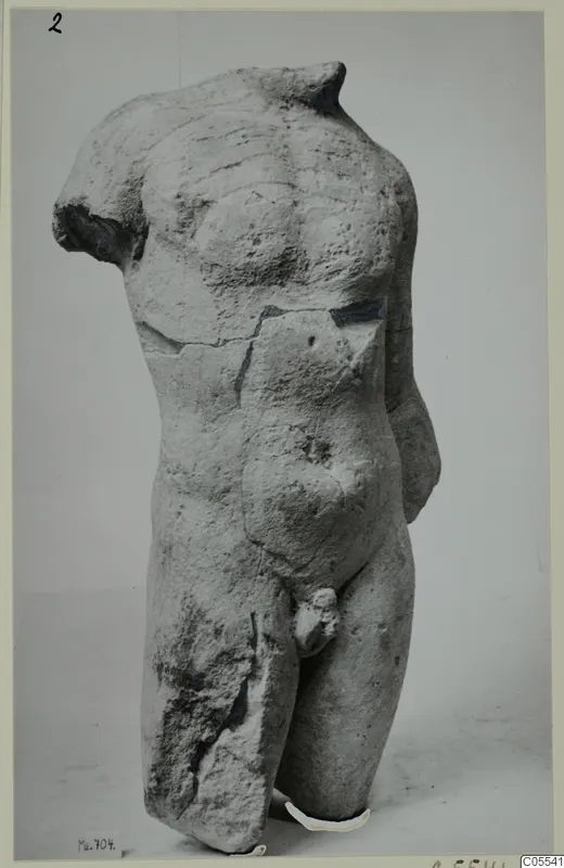 Limestone male torso from Mersinaki, headless and armless, photographed against a plain grey backdrop.