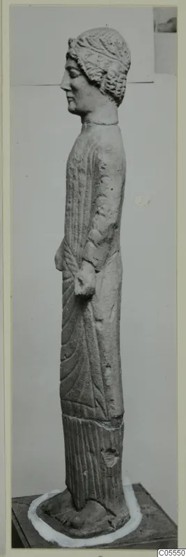 Limestone statue of a standing female figure, shown in profile facing left.